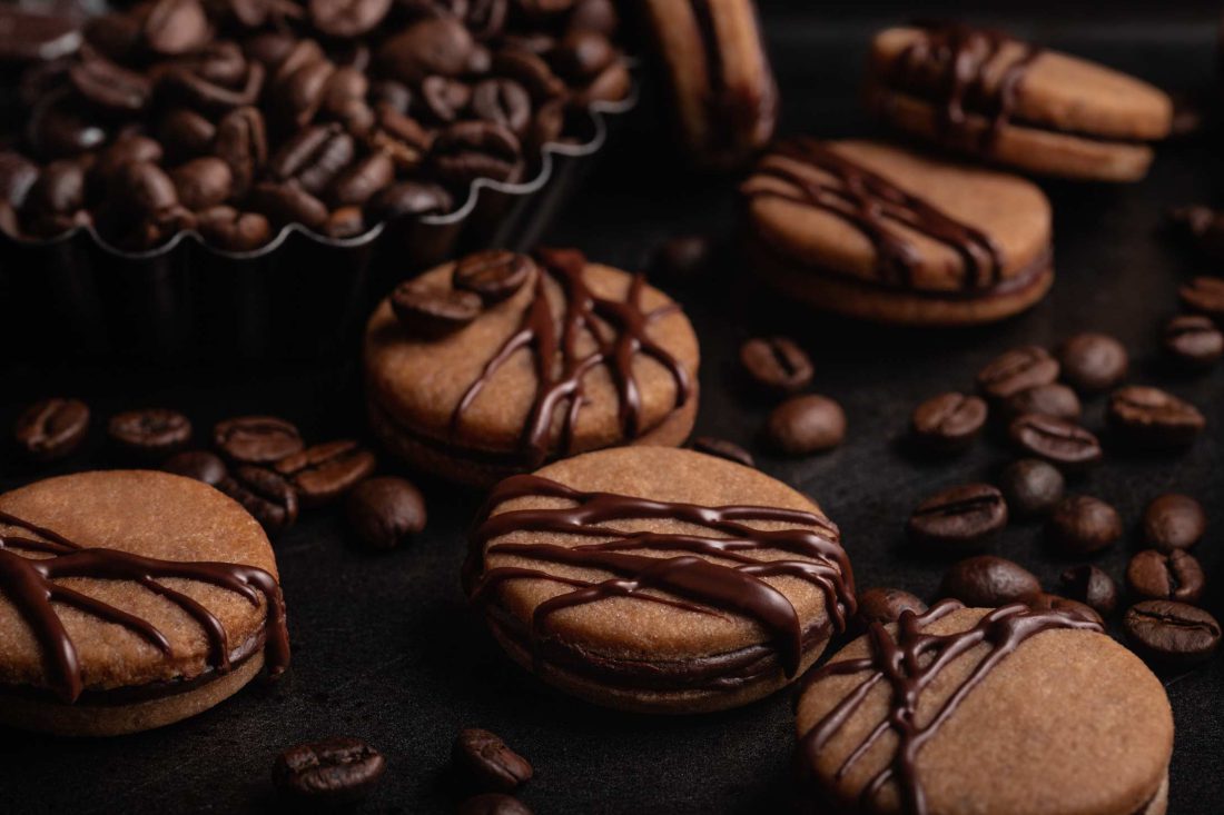 Gefüllte Kaffee Plätzchen mit Schokolade überzogen. Neben den Keksen steht ein Schälchen mit Kaffeebohnen.