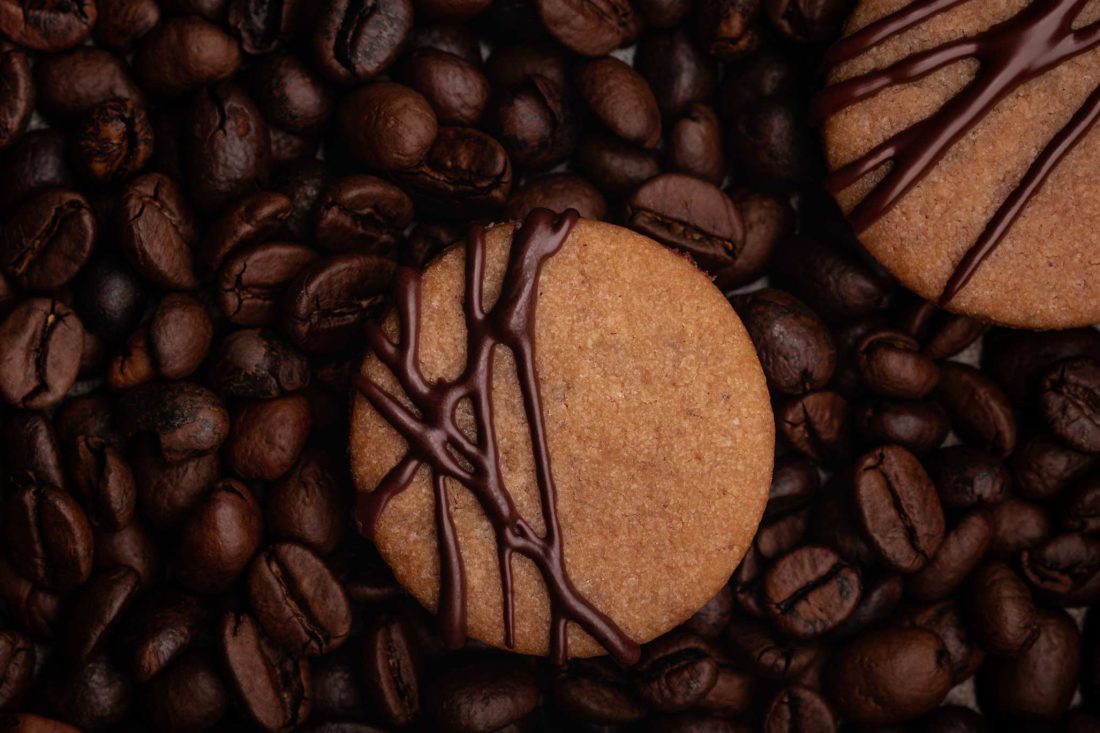 Zwei gefüllte Kaffee Plätzchen liegen auf einer Schicht aus frischen, ganzen Kaffeebohnen.