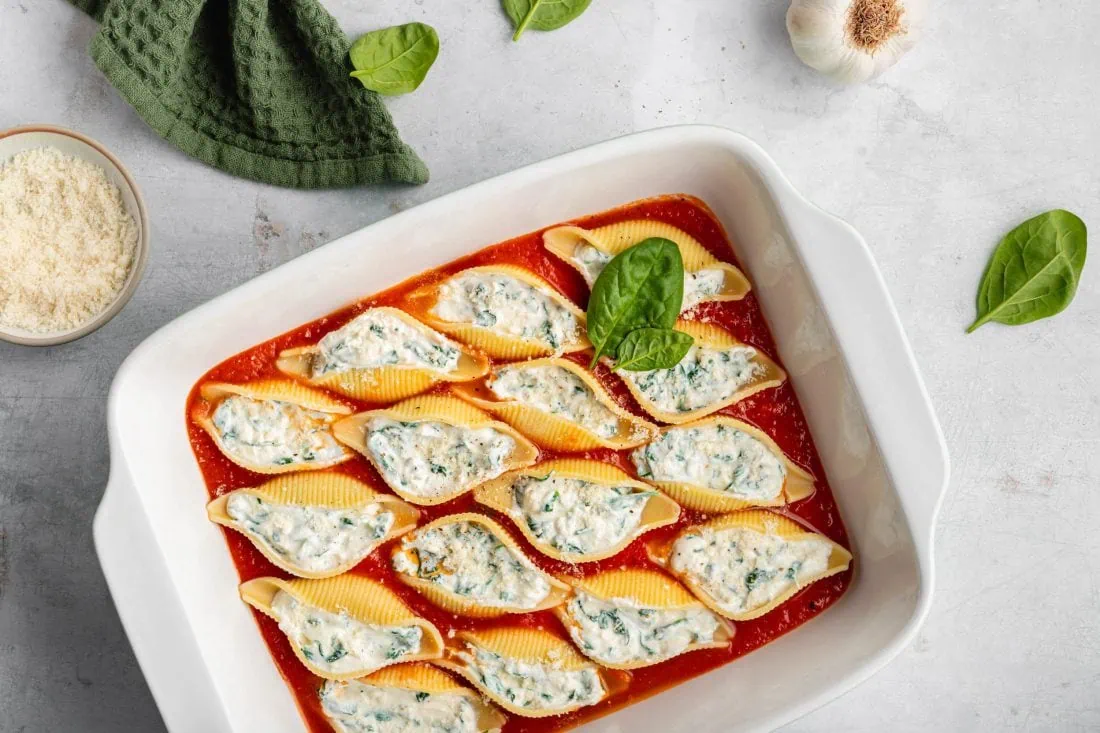 Gefüllte Muschelnudeln mit Ricotta und Spinat in einer Auflaufform. Neben der Form steht ein Schälchen mit geriebenem Parmesan.