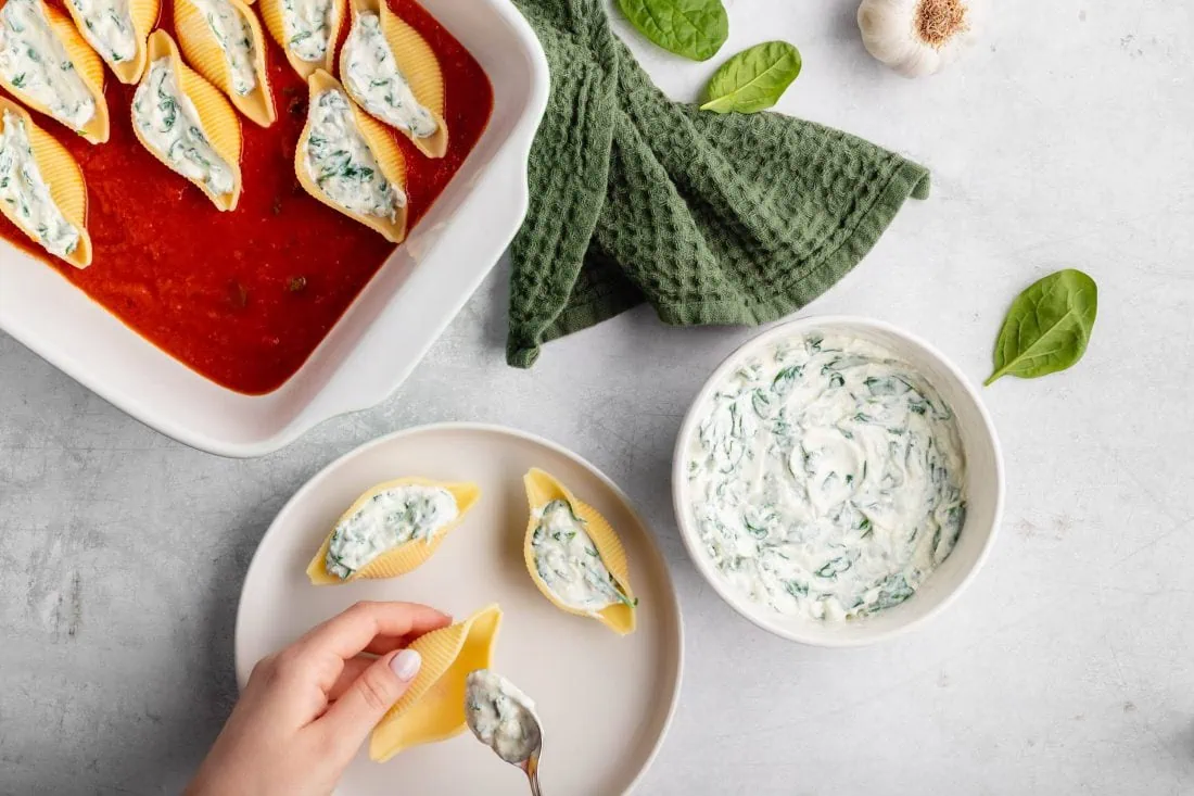 Die Muschelnudeln werden mit einer Ricotta-Spinat-Füllung befüllt und in eine Auflaufform mit Tomatensoße gelegt.
