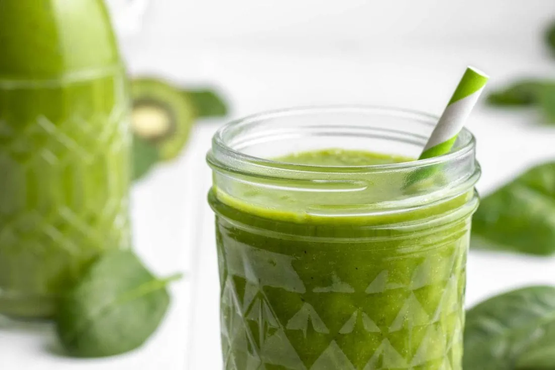 Grüner Smoothie mit Spinat, Banane und Mango in einem Schraubglas mit Strohhalm.
