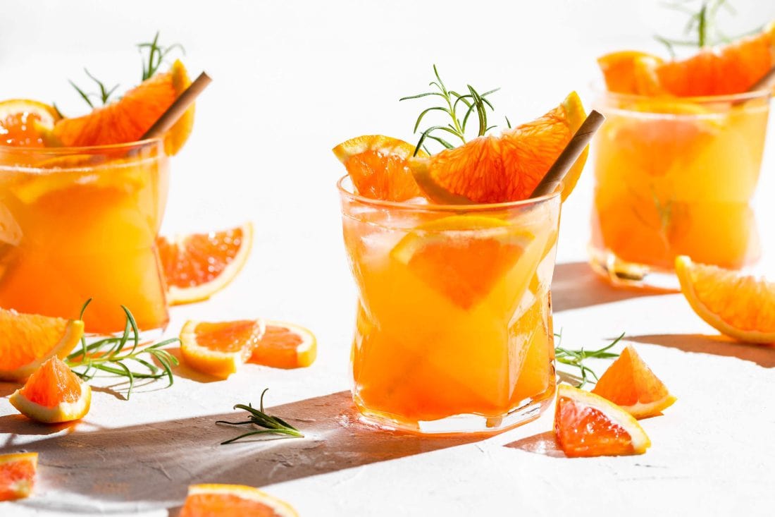 Orangener Aperitif mit Gin, Prosecco, Orangensaft & Aperol in schönen Gläsern, garniert mit frischem Rosmarin und Orange.