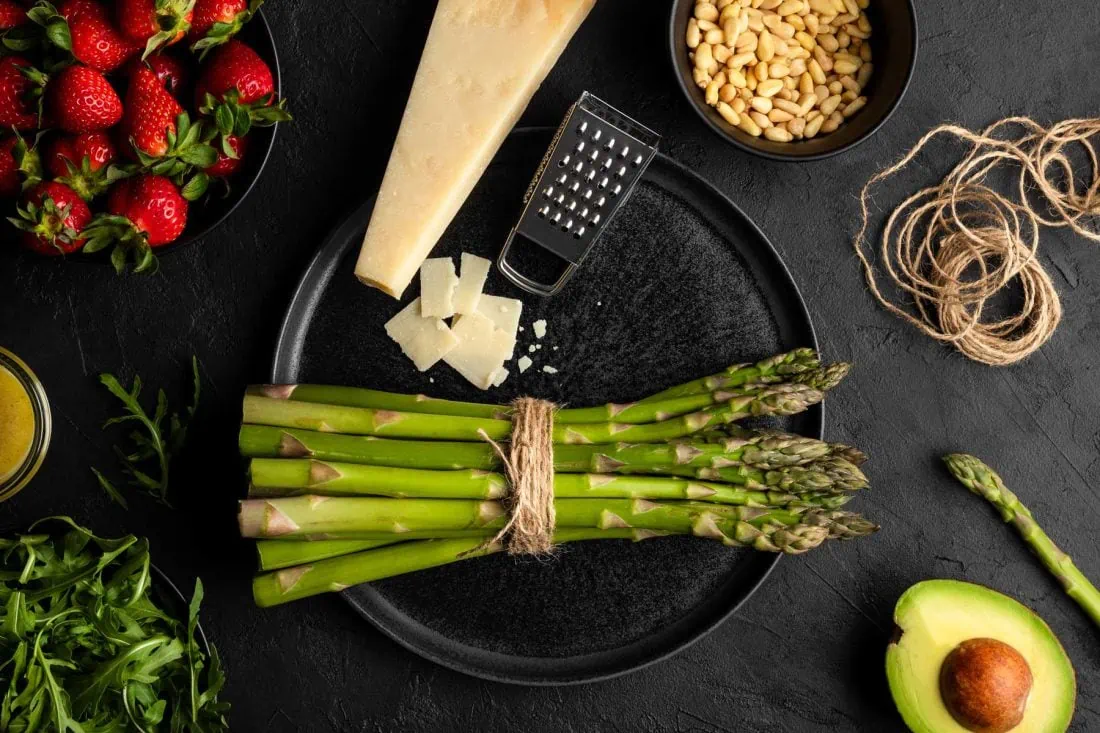 Alle Zutaten für den grünen Spargel-Salat im Überblick. Darunter sind: Spargel, Erdbeeren, Rucola, Avocado und Parmesan.