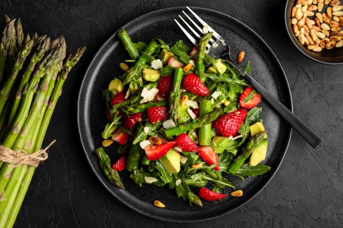 Grüner Spargel-Salat mit Erdbeeren und Avocado, bestreut mit Parmesan und gerösteten Pinienkernen.
