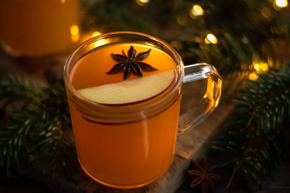 Heißer Apfelpunsch mit Amaretto in einer Tasse garniert mit Apfel und Sternanis auf einem Holzbrett.