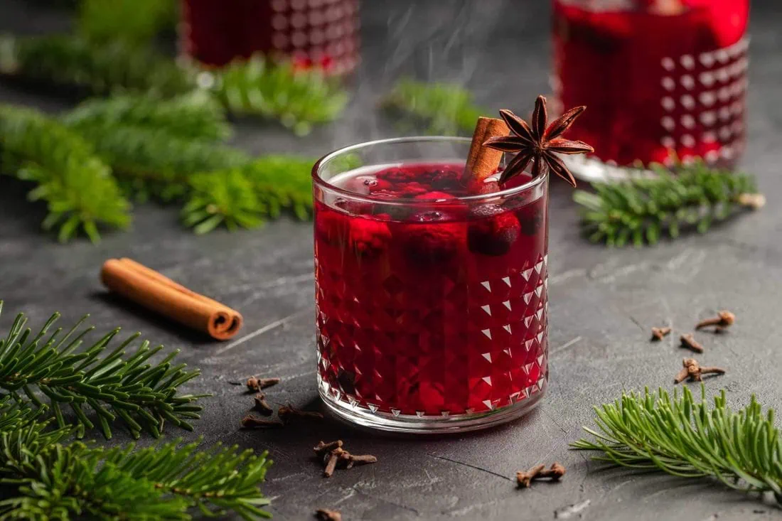 Lillet Hot Berry auf einem Tisch mit Tannenzweigen und Gewürzen daneben.