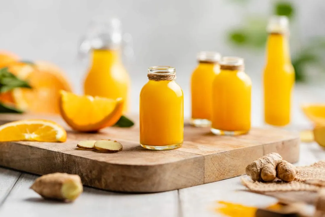 Mehrere selbstgemachte Immunbooster in kleinen Flaschen. DIe Ingwer-Orangen Shots stehen auf einem Holzbrett.