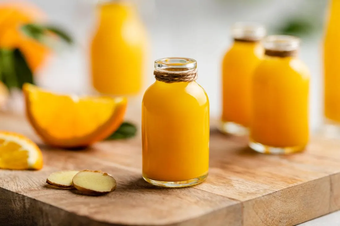 Ein Ingwer Shot mit Orange und Kurkuma in einre kleinen Flasche auf einem Holzbrett.