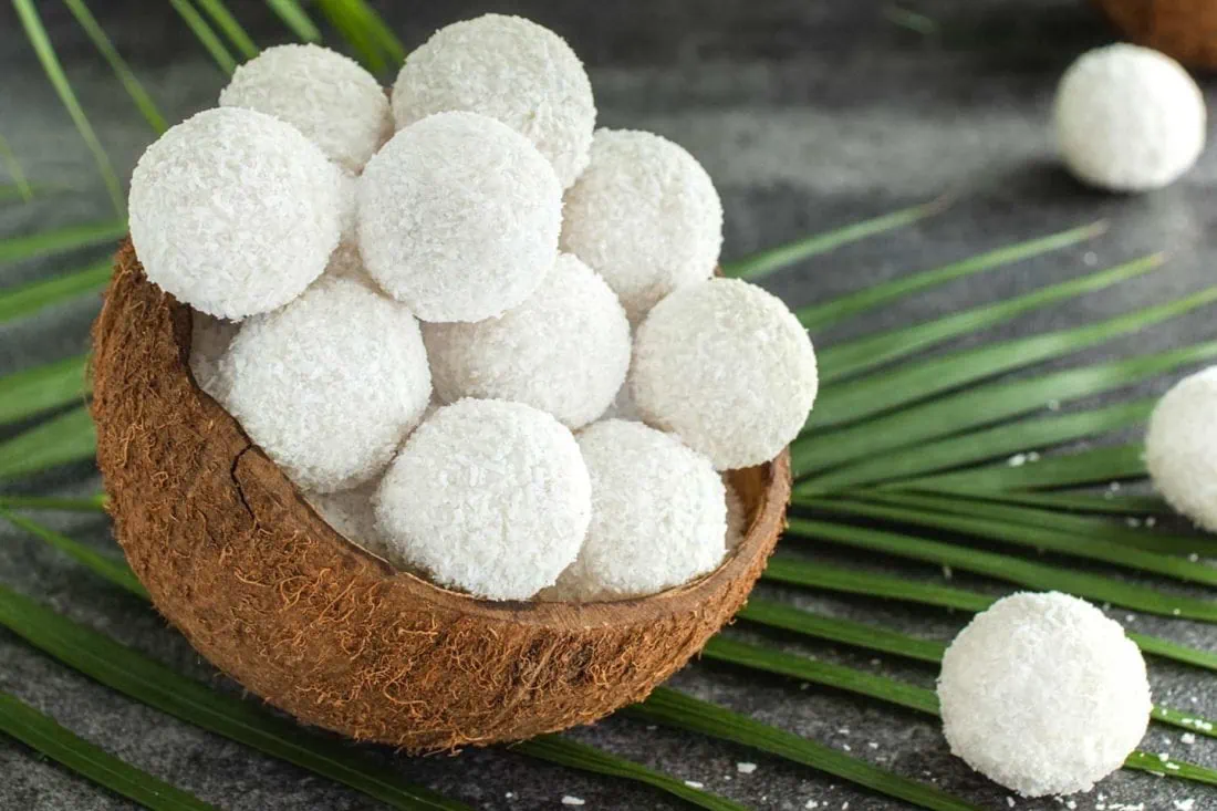 Kokospralinen bedeckt mit Kokosraspeln. Die Pralinen sind gestapelt in einer Schale aus einer halben Kokosnuss.