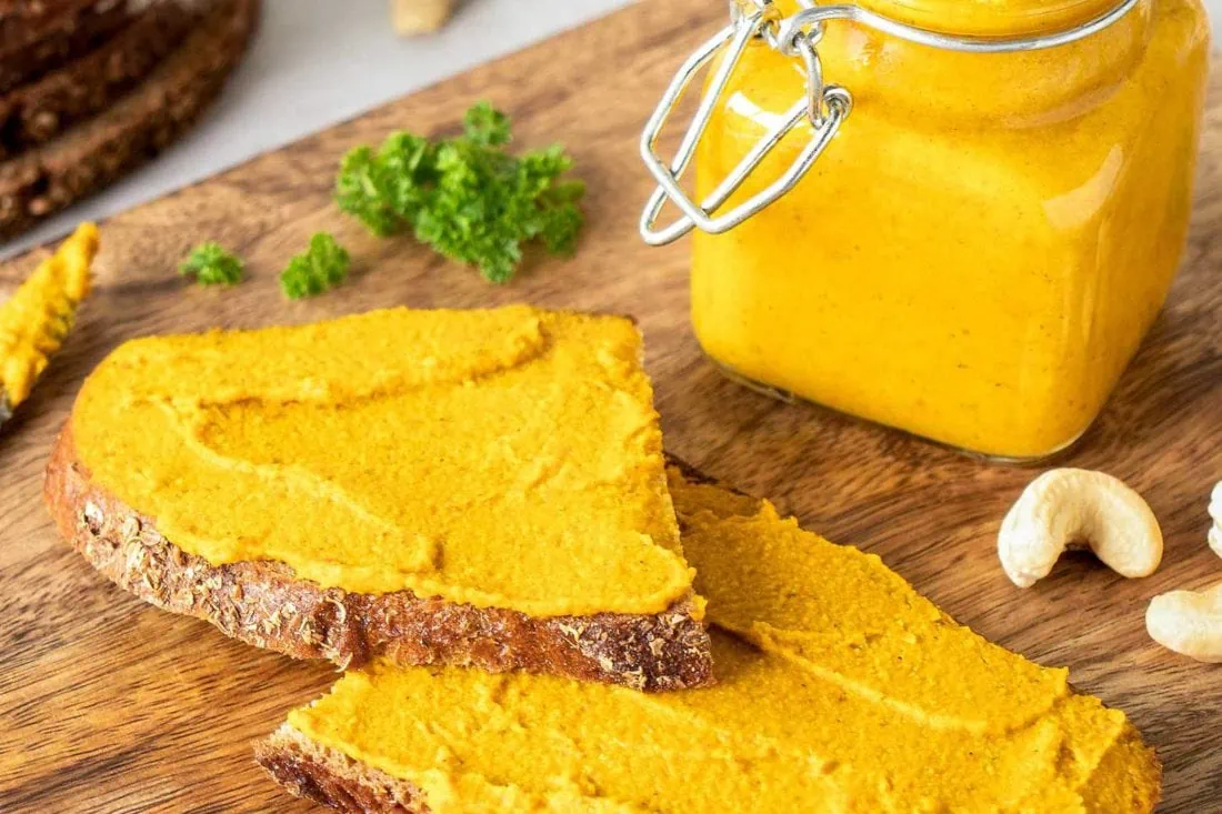 Kürbisaufstrich mit Cashews und Curry als veganer Aufstrich auf zwei Scheiben Brot.
