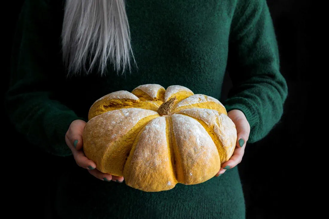 Kürbisbrot in den Händen einer Frau. Das Brot ist orange und hat die Form eines Kürbisses.