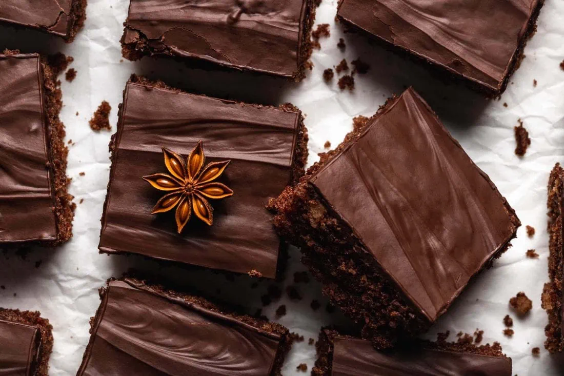 Einfache Lebkuchen von Blech mit einer Schokoglasur in quadratische Stücke geschnitten. Auf einem Stück liegt ein Sternanis.