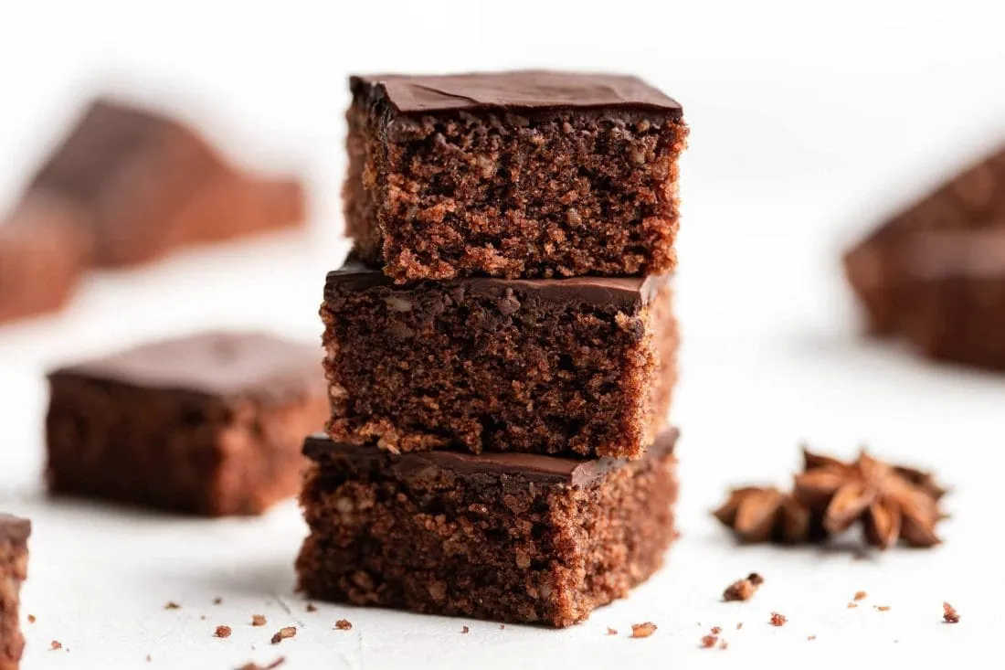 Lebkuchen vom Blech in Stücke geschnitten und aufeinander gestapelt. Von der Seite sieht man die Nüsse im Teig und die dicke Schokoladenglasur.