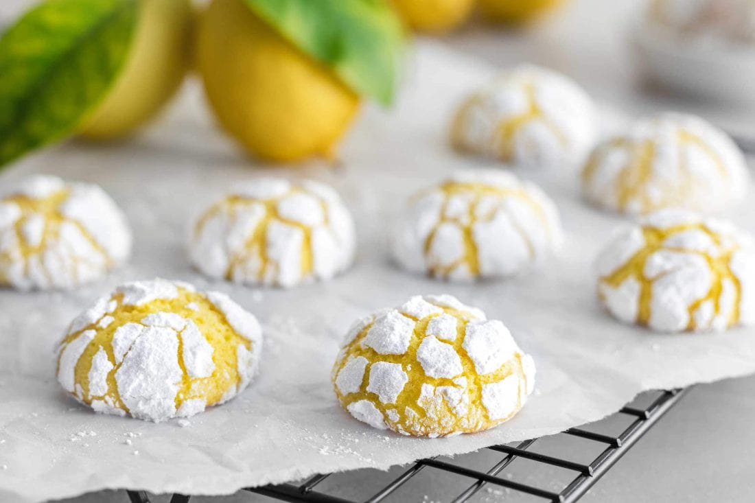 Lemon Crinkle Cookies auf einem Abkühlgitter. Hinter den Cookies liegen frische Zitronen.