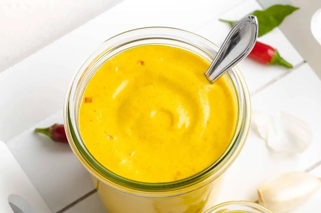 Mango Aioli mit Chili, aus Mayonnaise ohne Ei, in einem Glas. Neben der Soße liegen frische Chilis und Knoblauch.