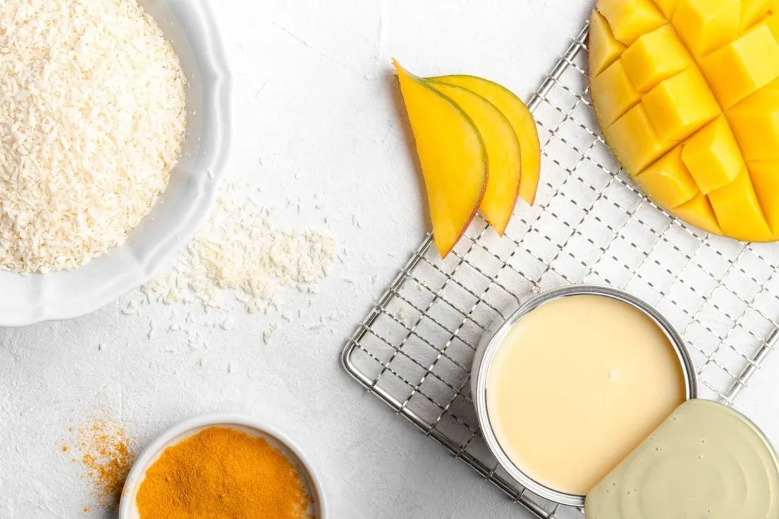 Alle Zutaten für die indische Süßigkeit Mango Ladoo bzw. Laddu auf einem Blick, wie gezuckerte Kondensmilch, Kokosraspeln und Mango.