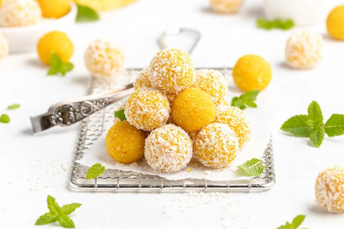 Mango Kokos Bällchen auf einem Gitter mit einem Papier drauf. Die Kugeln sind mit Kokosraspeln ummantelt.