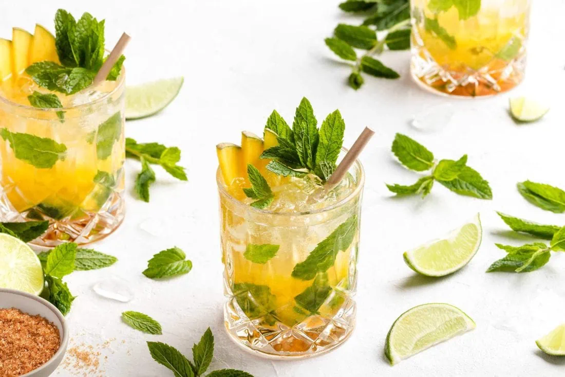 Mango Mojito in einem Glas garniert mit Mangostücken, frischer Minze und Limette.