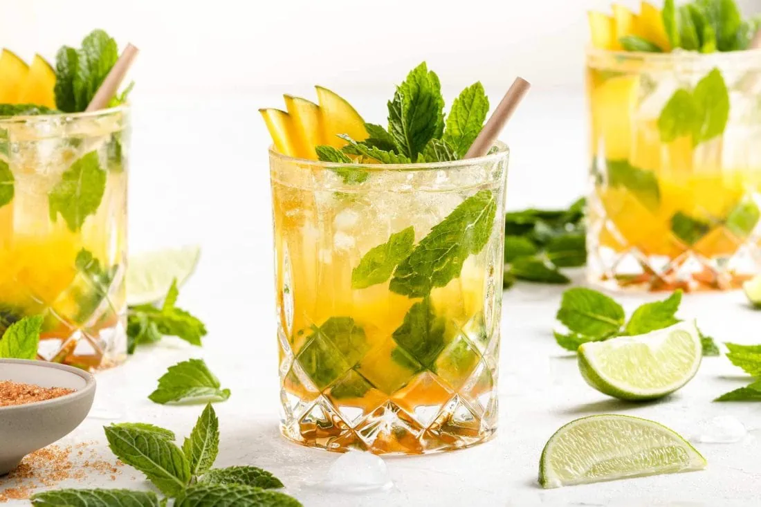 Mango Mojitos serviert in Tumblern garniert mit den verschiedenen Zutaten und einem Strohhalm.