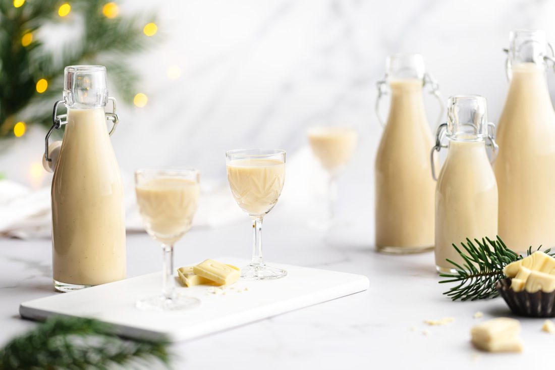 Mehrere Flaschen und Likörgläser gefüllt mit einem selbstgemachten Marzipan-Sahne-Likör mit Amaretto und weißer Schokolade.