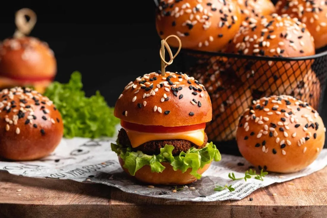 Mini Brioche Burger Buns und ein fertig belegter Fingerfood-Burger auf einem Holzbrett.