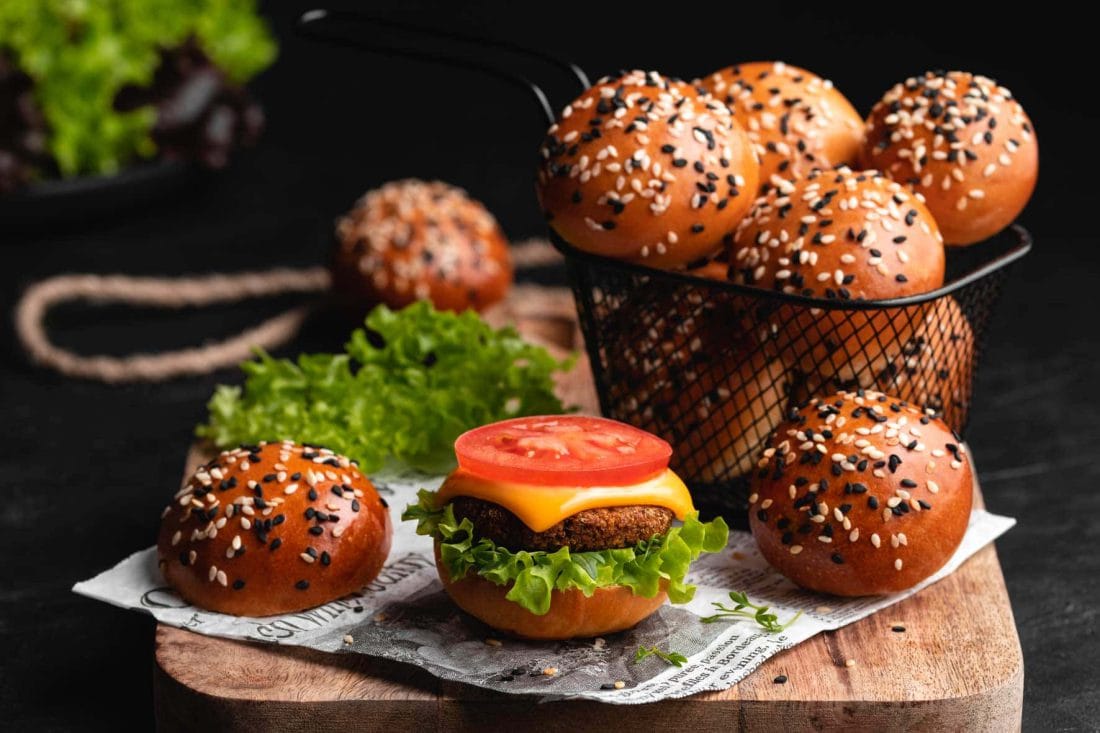 Mini Brioche Burger Bun belegt mit Salat, einem Falafel-Patty, Käse und Tomate auf einem Holzbrett.