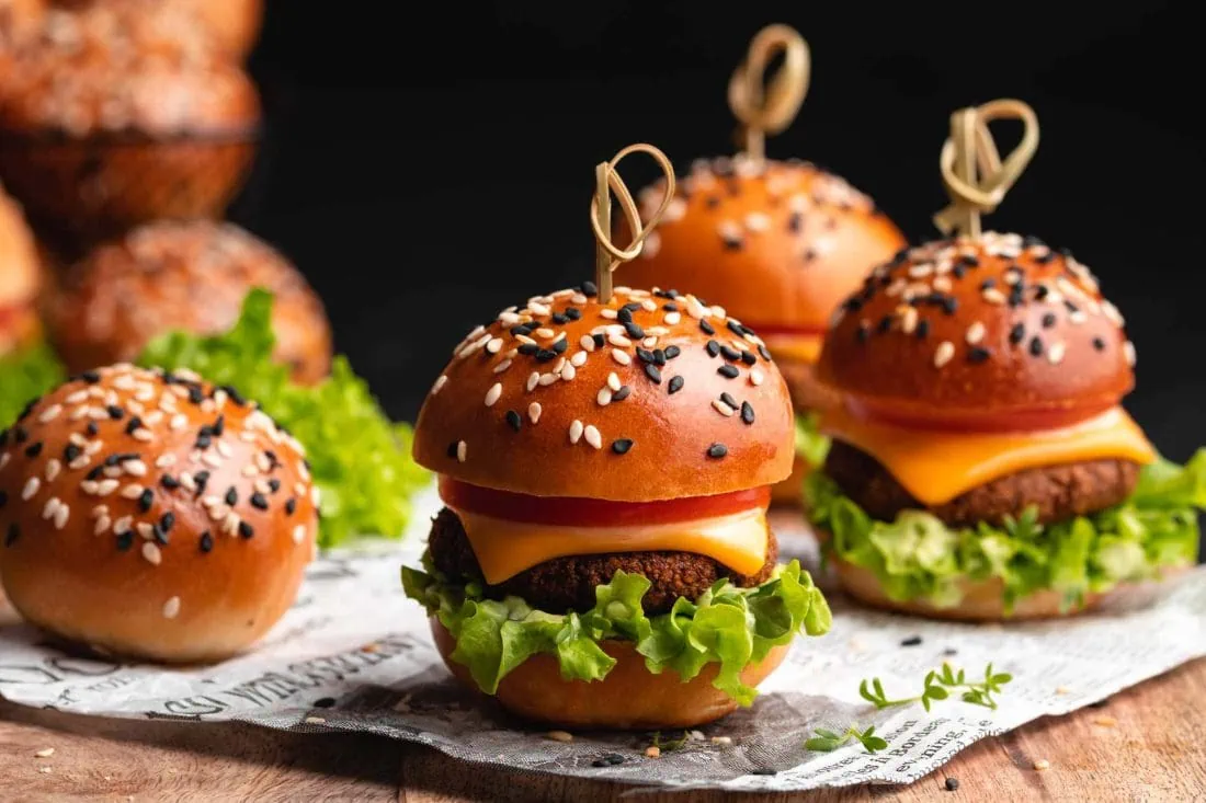 Mini Burger belegt mit einem Patty, Salat, Käse und Tomate auf einem Holzbrett.