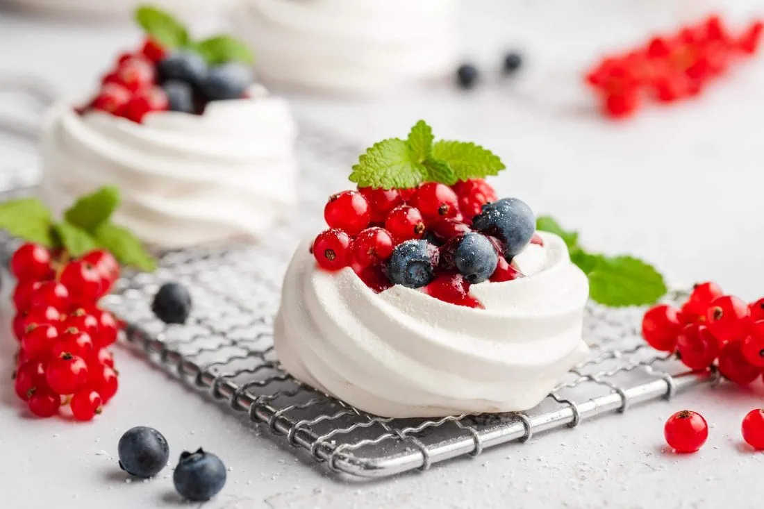 Zwei Mini Pavlova auf einem Gitter. Die Pavlova Törtchen sind als Dessert mit frischen Beeren garniert.