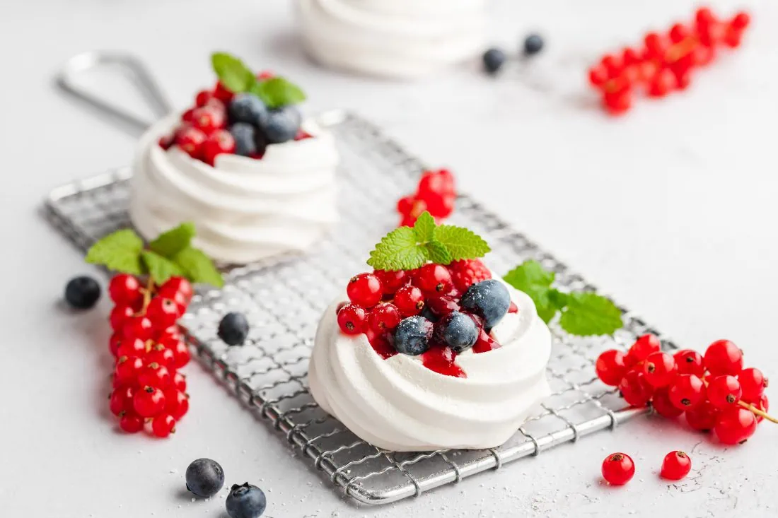 Mini Pavlova gefüllt mit Mascarpone und einer Beerensauce auf einem Abkühlgitter.
