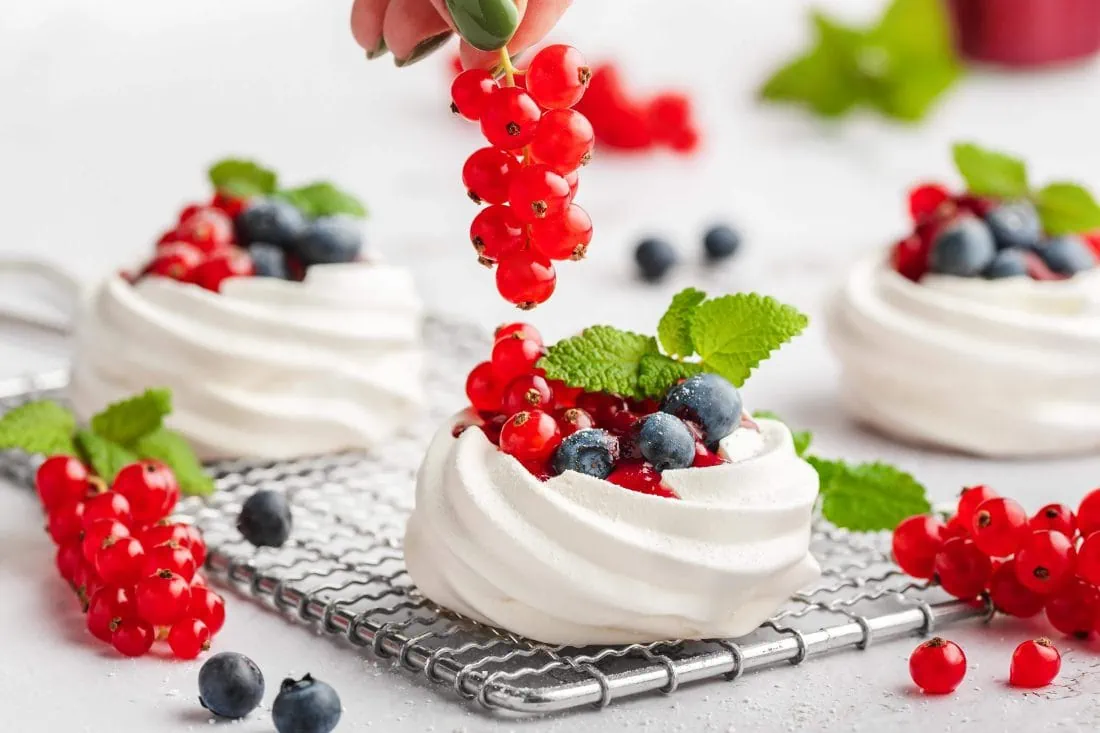 Auf eines der drei Mini Pavlova wird gerade als Garnitur ein Zweig frische Johannisbeeren gelegt.