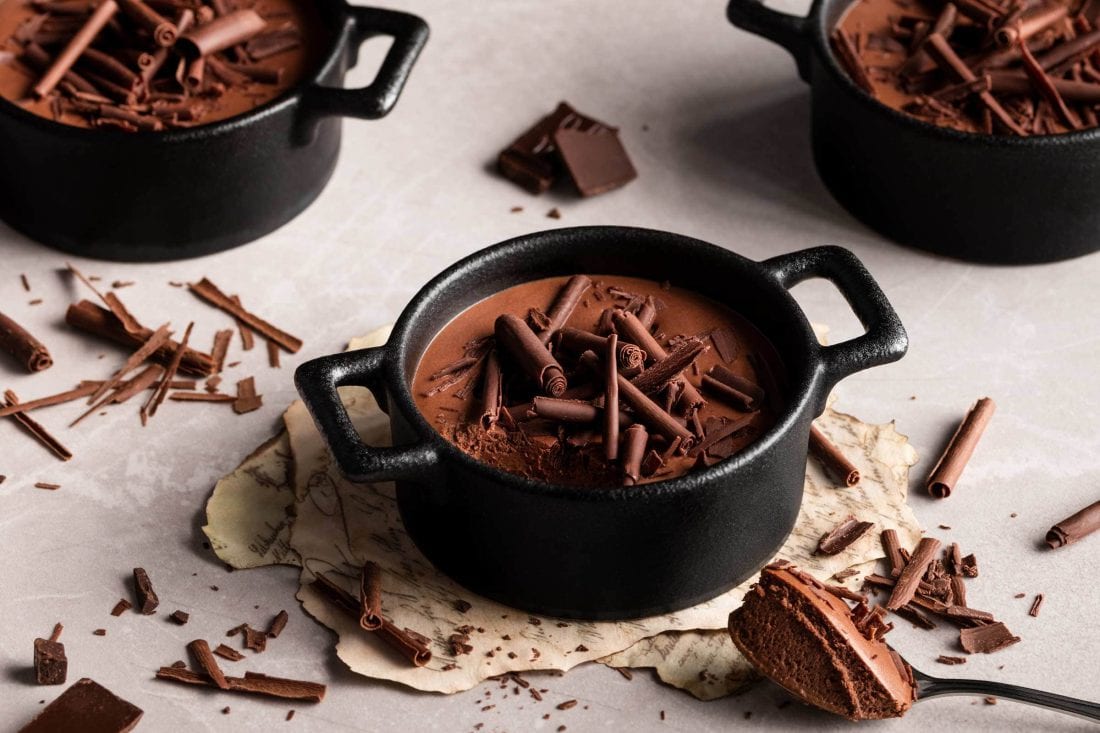 Luftige Mousse au Chocolat garniert mit Schokoladenstücken und einem Löffel daneben.