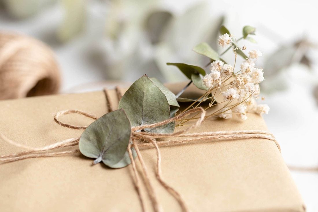 Ein Geschenk in braunem Papier verpackt mit einer Schleife und getrockneten Blumen.