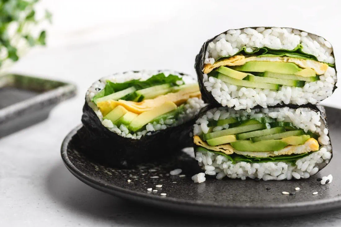 Drei Hälften der Sushi Sandwichs serviert auf einem schwarzen Teller.