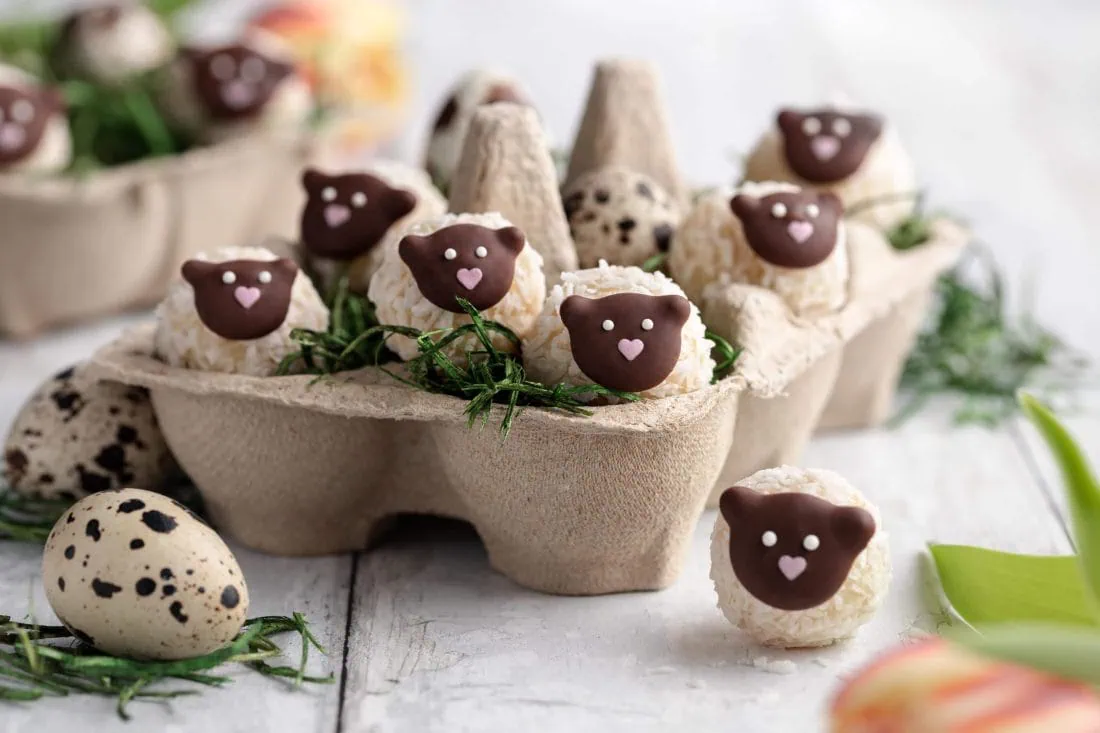 Ein Osternest mit mehreren kleinen Osterpralinen in Schafform aus weißer Schokolade mit süßen Gesichtern.