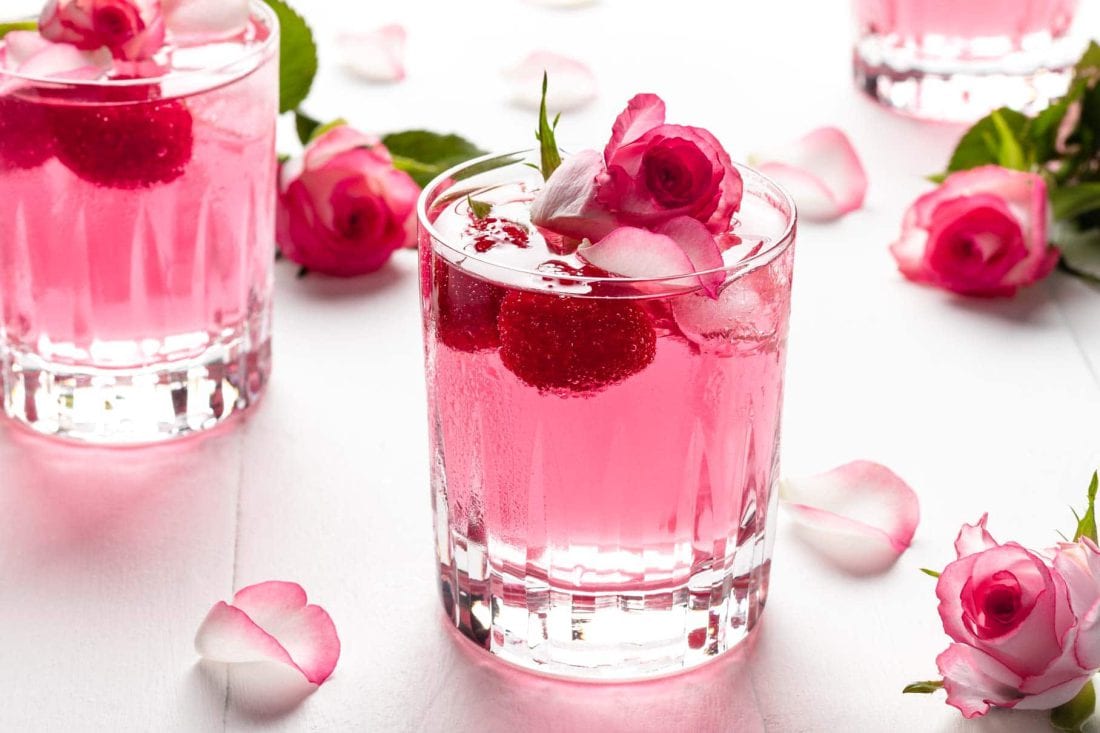 Pinker Gin Wild Berry mit Rosenwasser garniert mit frischen Himbeeren und Rosenblüten.