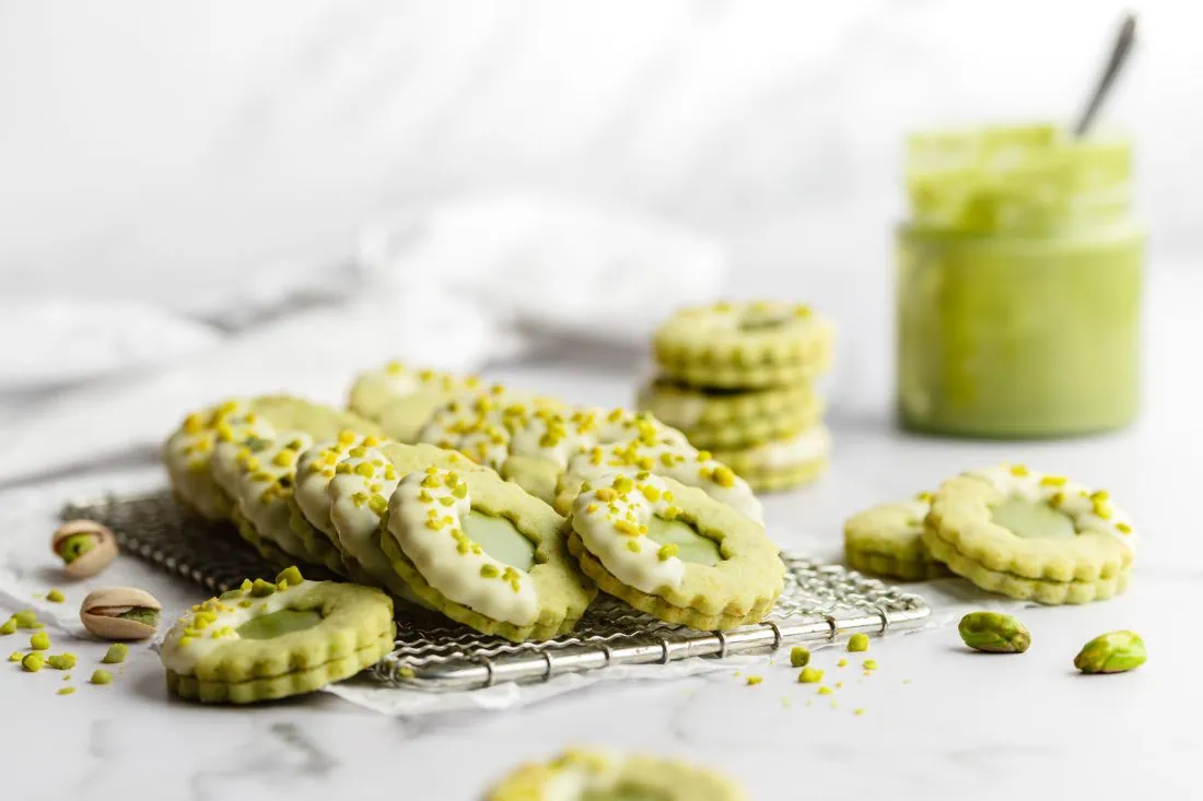 Grüne Plätzchen mit gehackten Pistazien und einer Füllung aus Pistaziencreme und Garnitur aus weißer Schokolade.