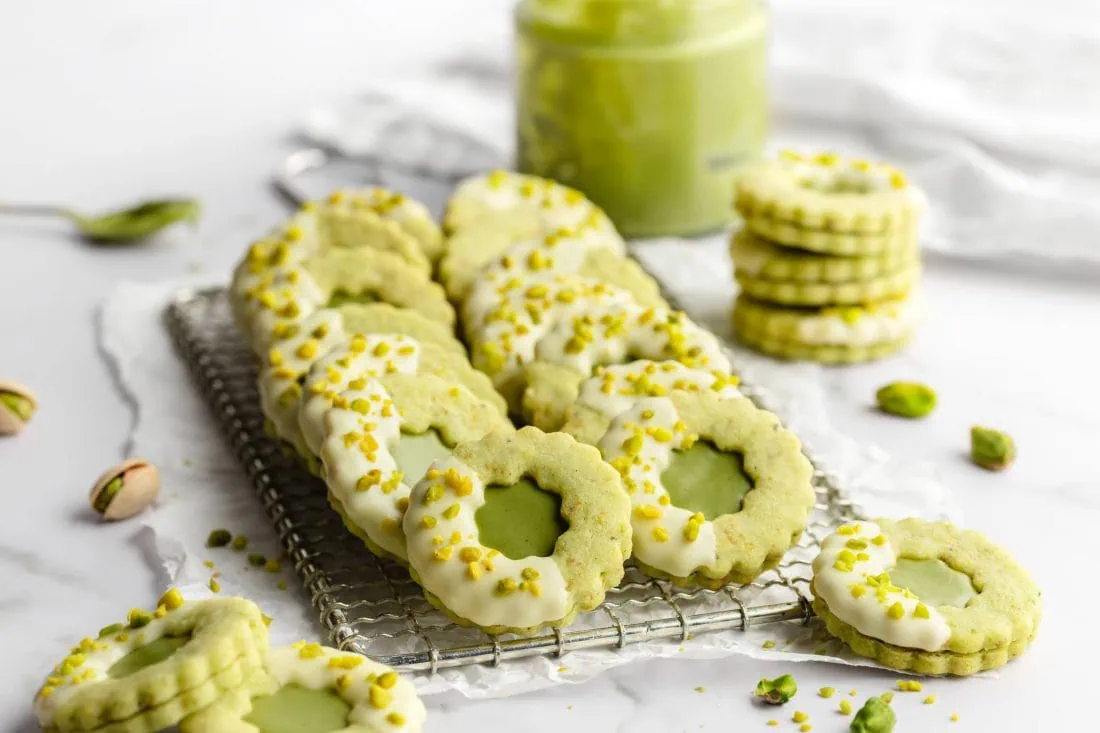 Pistazien-Kekse mit einer Pistaziencreme-Füllung und weißer Schokolade liegen auf einem Kuchengitter.