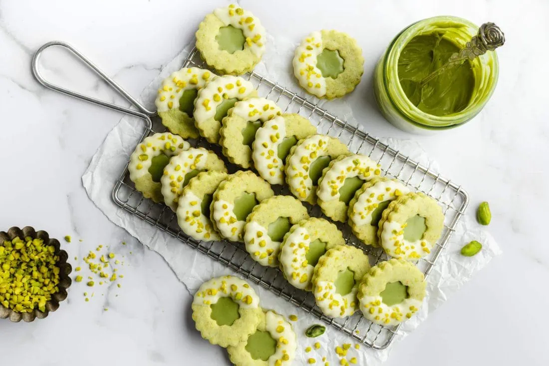 Mehrere Pistazien-Plätzchen liegen zum Trocknen der weißen Schokolade auf einem Gitter.