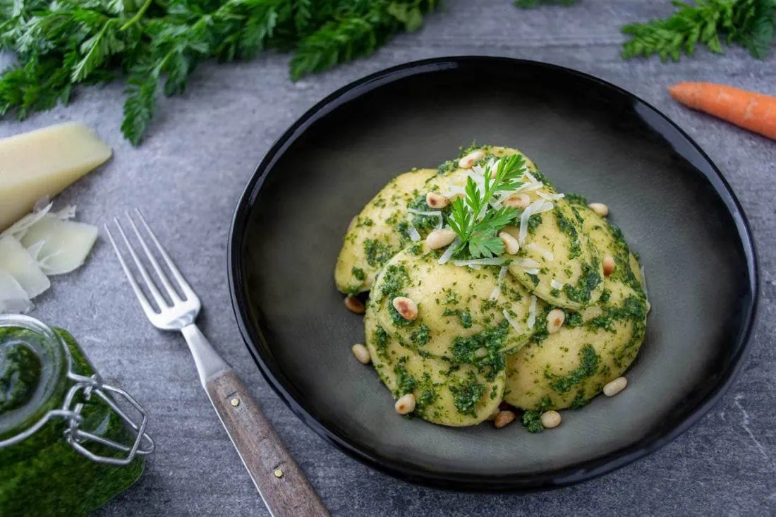 Ravioli mit Ricotta-Karotten-Füllung in einem tiefen Teller mit Pesto aus Karottengrün.