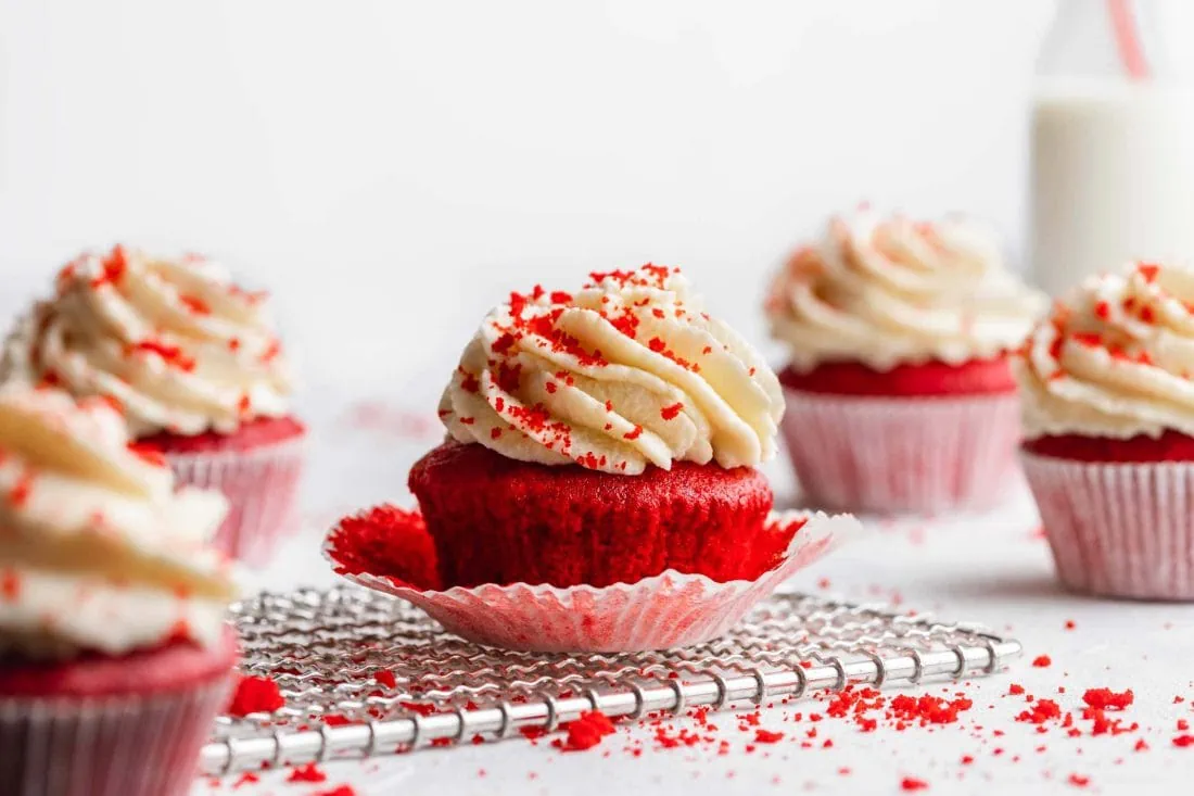 Mehrere Red Velvet Cupcakes mit hellem Frosting. Das Papier des mittleren ist abgelöst.