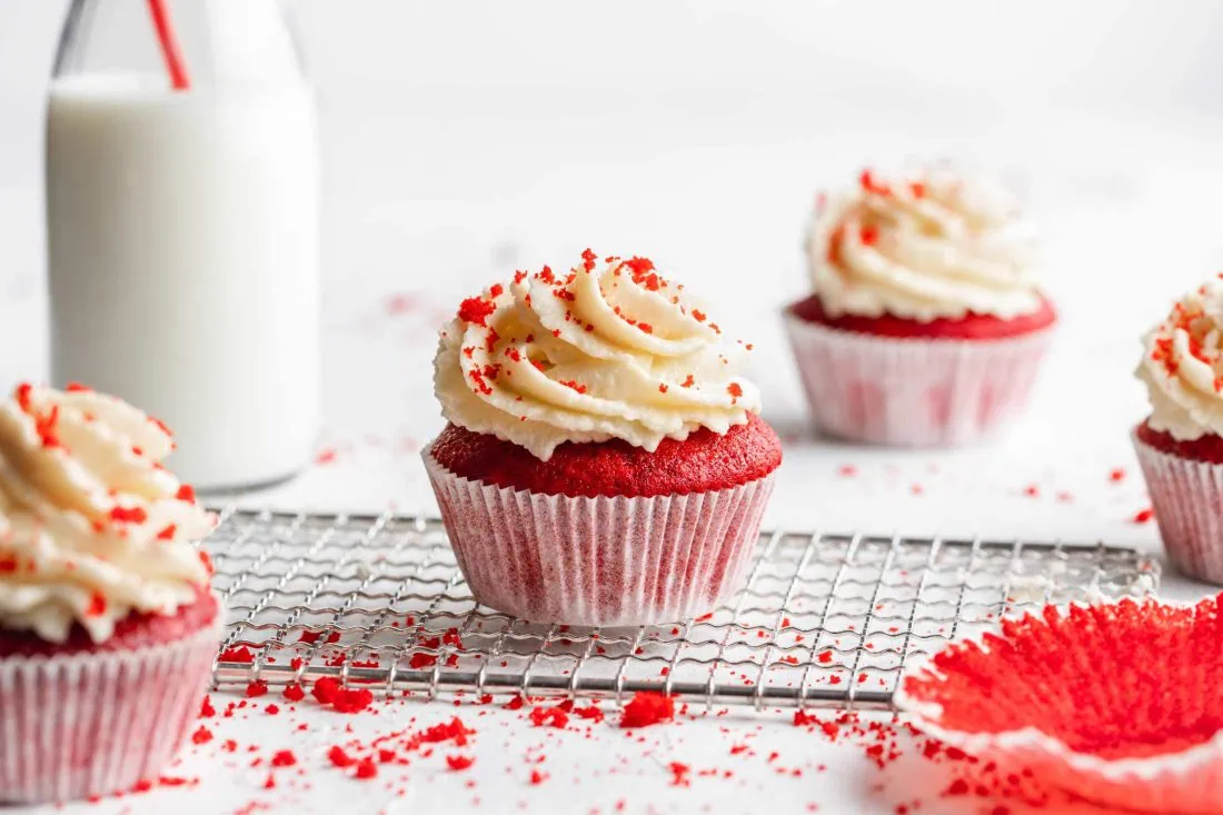 Mehrere Red Velvet Cupcakes auf einem hellen Untergrund. Im Hintergrund steht eine Flasche Milch.