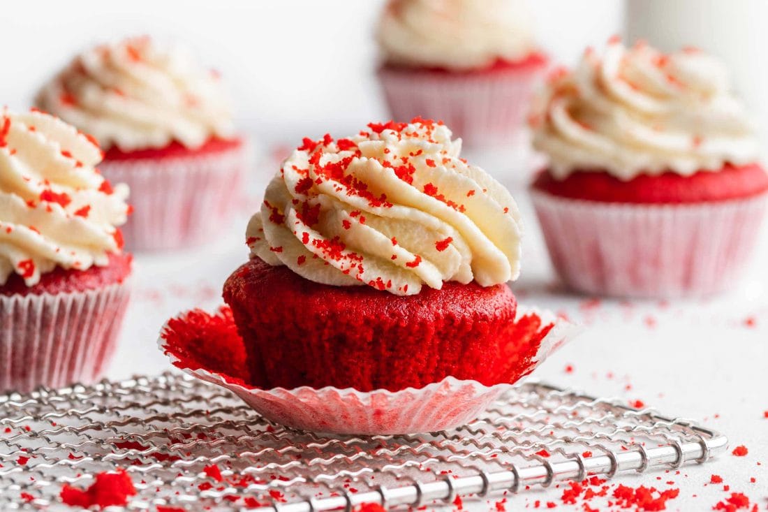 Im Vordergrund ist ein knalliger Red Velvet Cupcake mit fast abgelösten Muffinpapier.