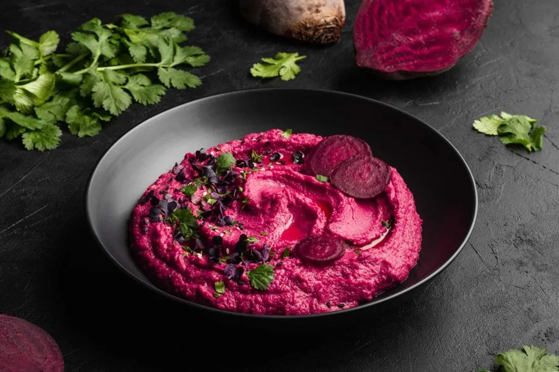 Rote Bete Hummus in einer Schüssel getoppt mit frischer Kresse, Sesam und Olivenöl.