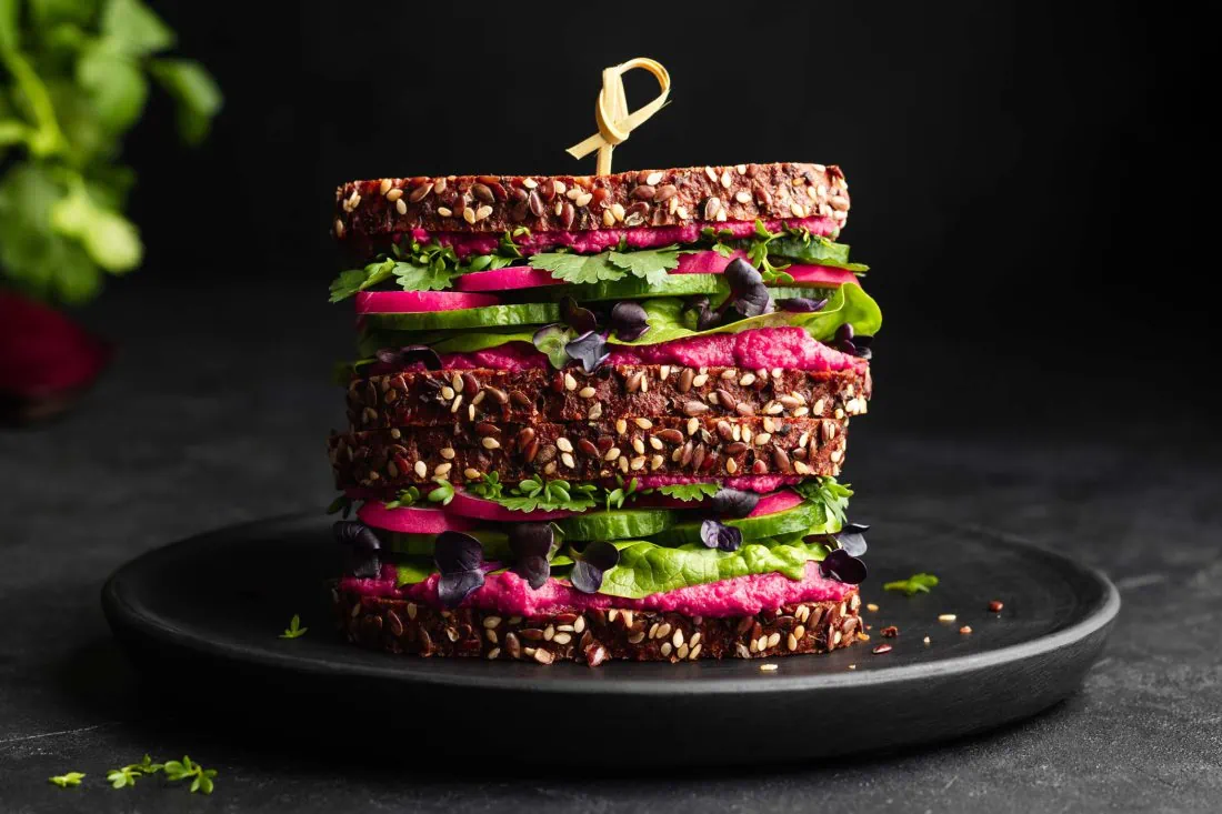 Rote Bete Hummus Sandwich belegt mit frischem Salat, Radieschen, Gurke und Kresse.