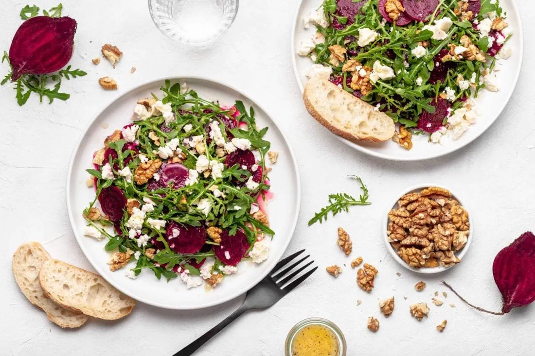 Rote Bete Salat bestehend aus Rucola, Walnusskernen, Schafkäse und einem Honig-Dressing auf runden Tellern.