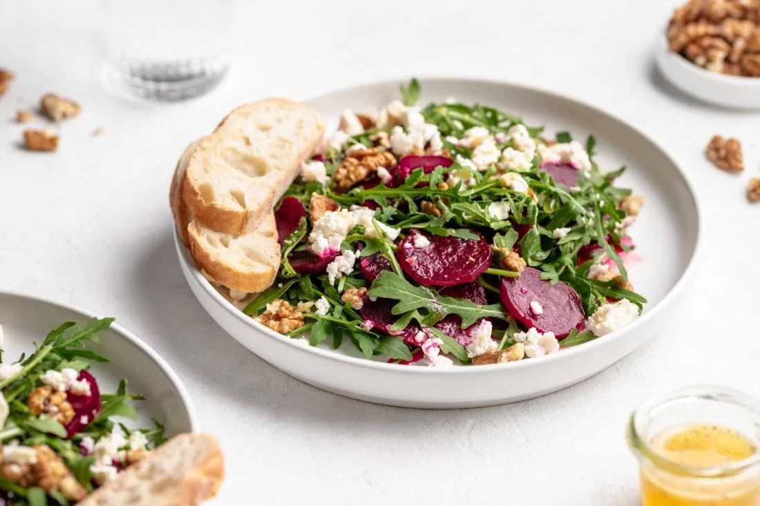 Rote Bete Salat verfeinert mit Schafkäse und gehackten Walnusskernen serviert auf einem weißen Teller.