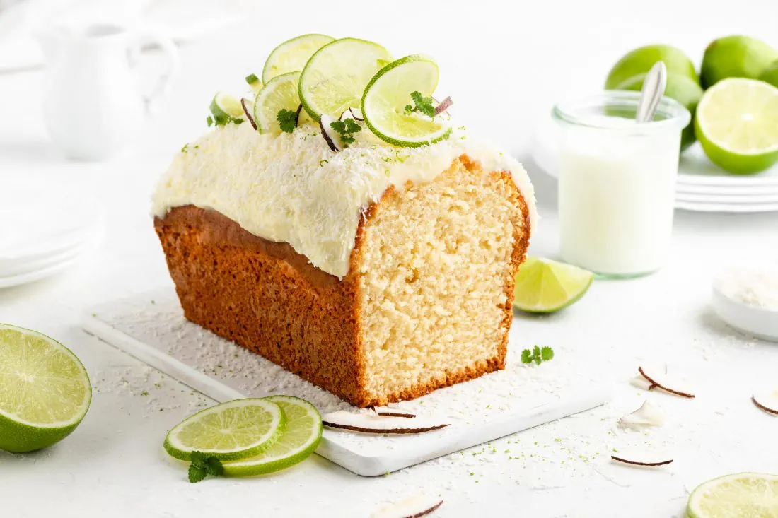 Ein Kastenkuchen mit Limette und Kokos getoppt mit einem cremigen Frischkäse-Frosting, Limettenscheiben und Kokosraspeln.