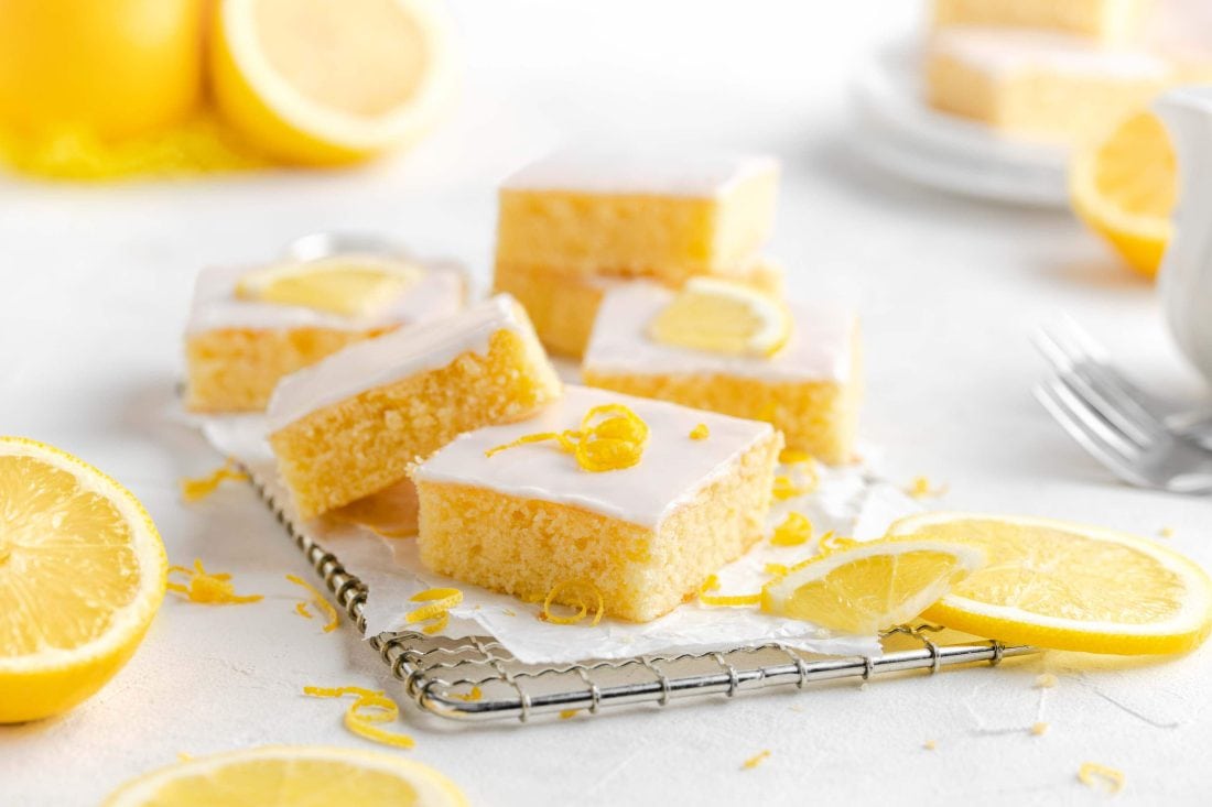 Der geschnittene, saftige Zitronen-Buttermilchkuchen mit Zuckerguss liegt auf einem kleinen Gitter mit weißem Papier darunter.