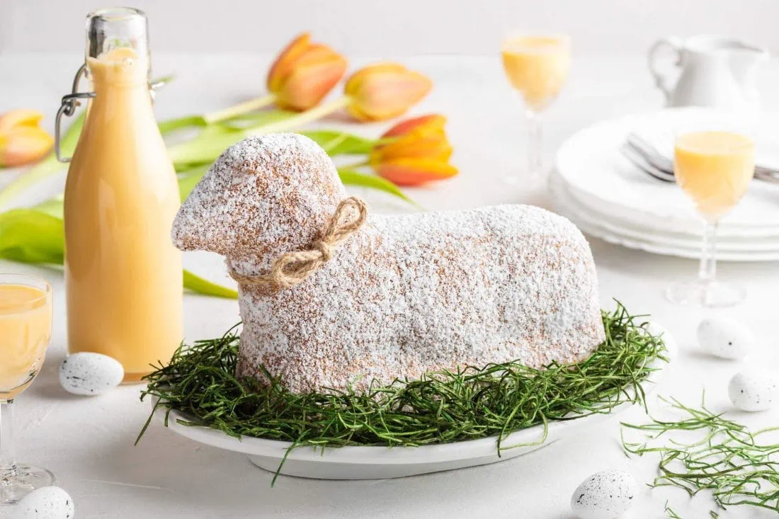 Ein saftiges Osterlamm mit Eierlikör, bestreut mit Puderzucker und einer Schleife, liegt auf einem Teller.