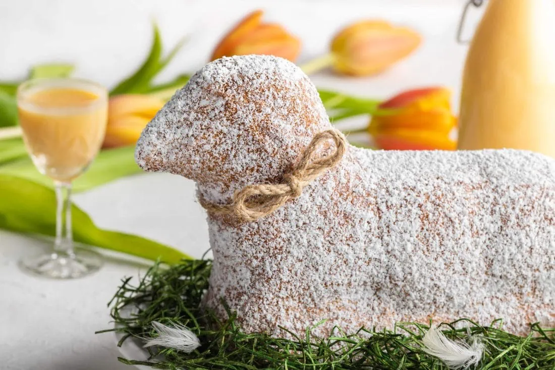 Ein saftiges Osterlamm mit Eierlikör, eine Flasch und mehrere gelbe Tulpen liegen auf einem Tisch.